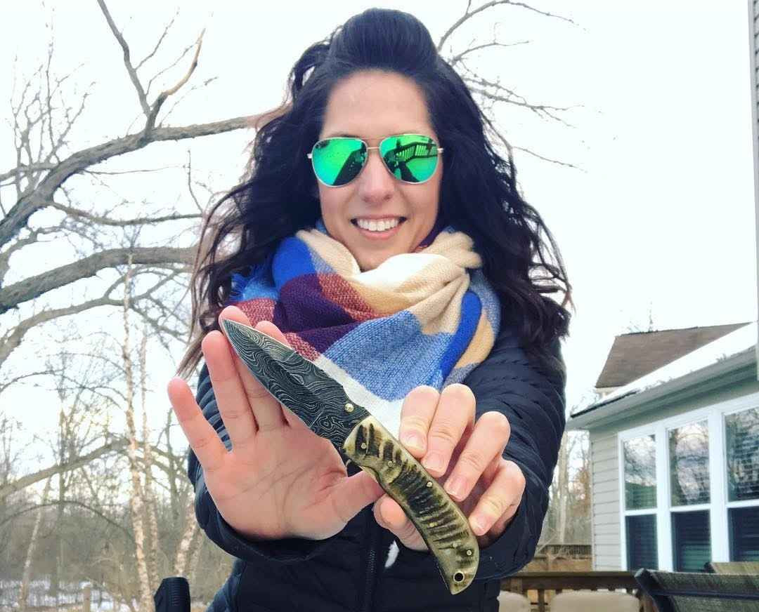 Person holding a knife outdoors with trees and a house in the background