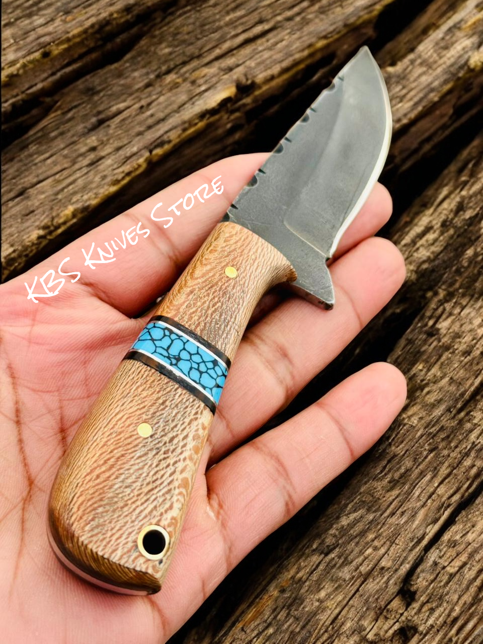 Hand holding a knife with a wooden handle and turquoise inlay on a wooden surface.
