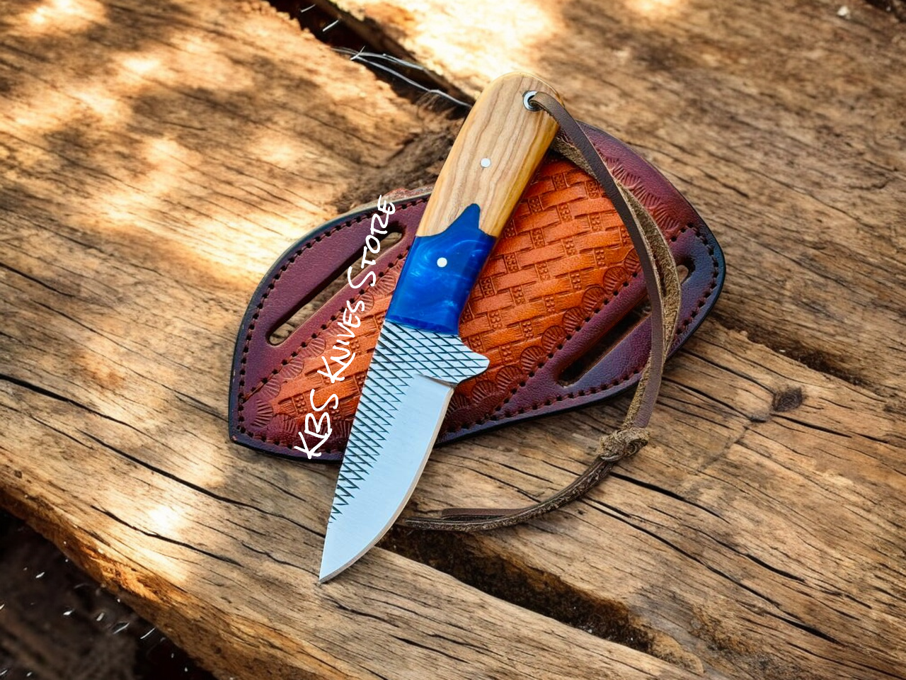 Cowboy Carry Knife with a wooden handle and blue blade in a leather sheath on a wooden surface