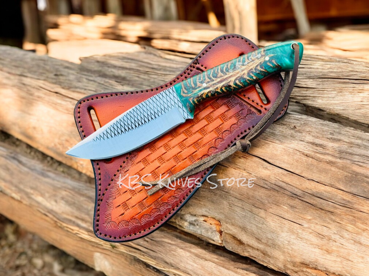 Knife with decorative sheath on a wooden surface, branded 'KBS Knives Store'.