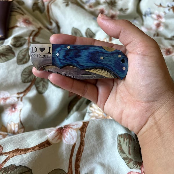 Hand holding a personalized pocket knife with a floral patterned fabric background