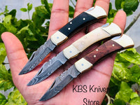 A trio of exquisite folding pocket knives with Damascus steel blades, featuring handles made from buffalo horn, bone, and rosewood, adorned with brass bolsters. Each knife measures 5 inches overall and comes with a stylish leather case for secure storage and portability.