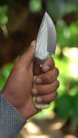Drop point blade of a Damascus steel field dressing knife with leather sheath.
