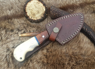 Damascus steel drop point skinning knife displayed outdoors, demonstrating its practical use in the field.
