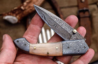 Custom handmade Damascus steel folding knife featuring water buffalo horn handle and detailed Damascus bolsters.